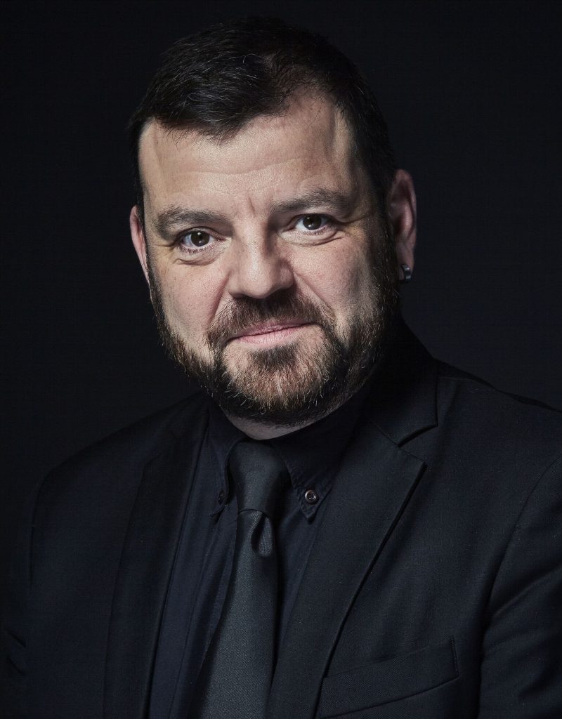 Steven Devine, conductor and harpsichordist, short brown hair with a beard.
